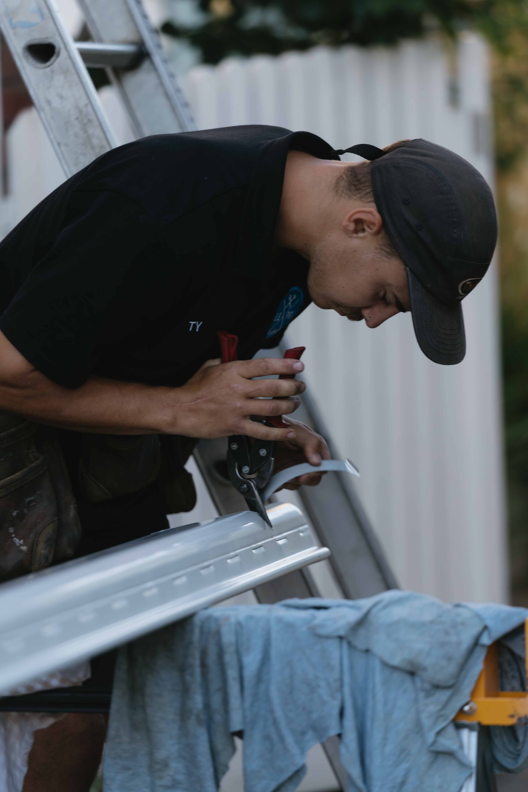 A tradesman closely cutting or adjusting a piece of metal flashing on a workbench outdoors. DB Pro Plumbing.